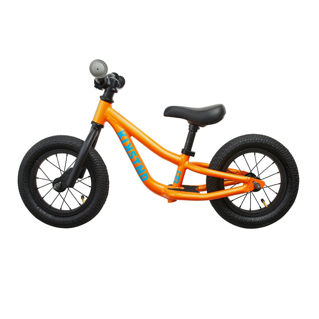Side view of orange balance bike for kids. White background. 